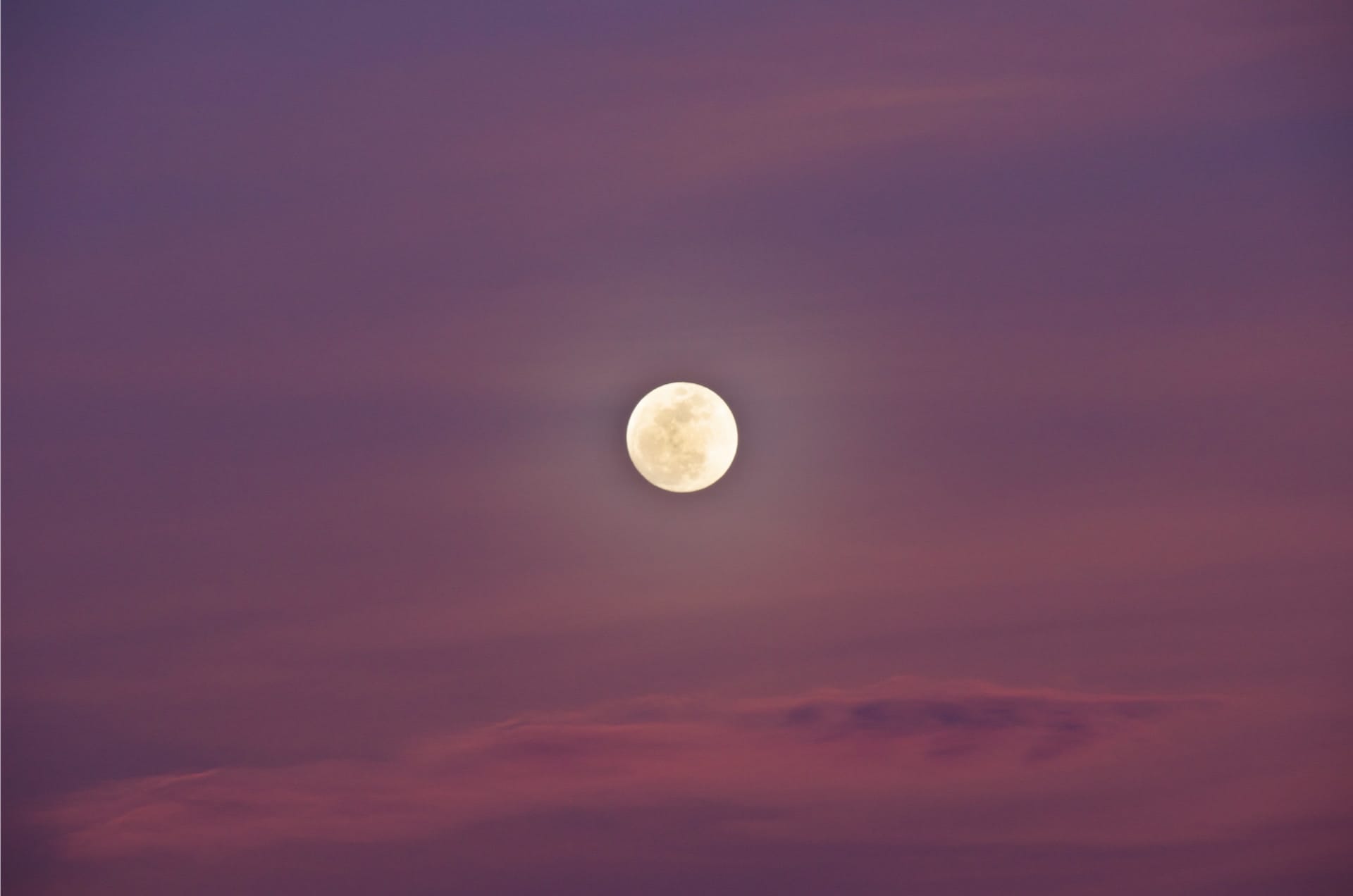 A super blue blood moon rising at dusk over the Sandia Mountains in Albuquerque, New Mexico. The sky is painted in shades of pink, enhancing the moon's striking appearance against the evening backdrop. This rare lunar event adds a serene yet powerful element to the landscape.